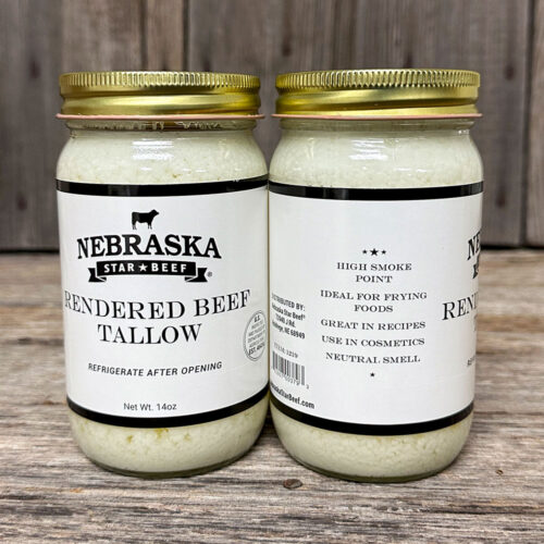 Two jars of Nebraska Star Beef rendered beef tallow on a wooden surface, front label visible: 'Rendered Beef Tallow' with gold lids nearby.