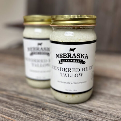 Two glass jars of rendered beef tallow on a wooden surface; front jar shows the Nebraskan Star Beef label with a cow silhouette and gold lid.